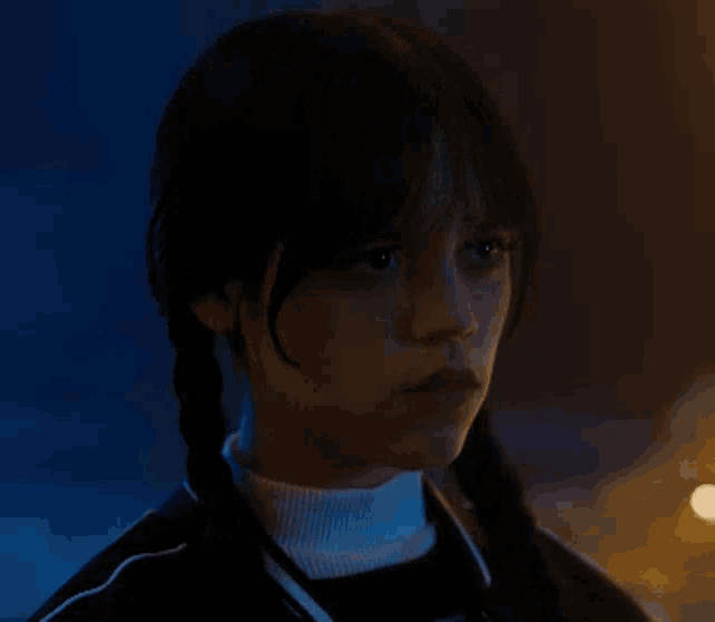a young girl with pigtails and a turtleneck is looking at the camera .