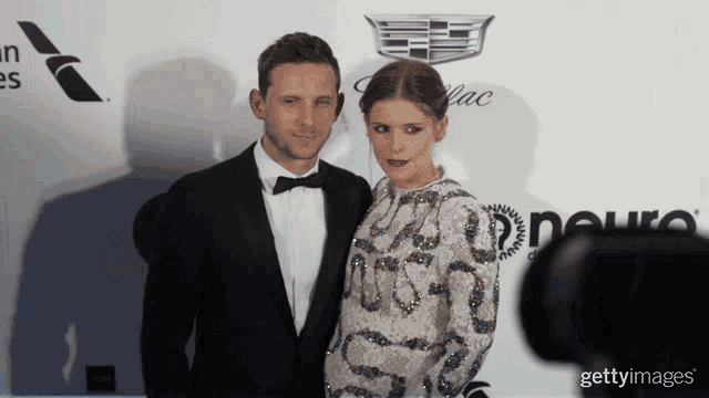 a man in a tuxedo and a woman in a white dress pose for a picture