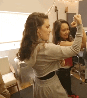 two women are dancing in a room with a guitar on the wall behind them