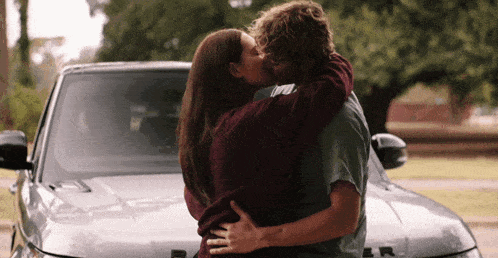 a man and a woman kissing in front of a silver car