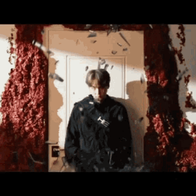 a man in a black jacket is standing in front of a door with bullets flying around him .