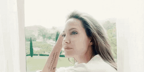 a woman with a tattoo on her wrist is standing in front of a window .