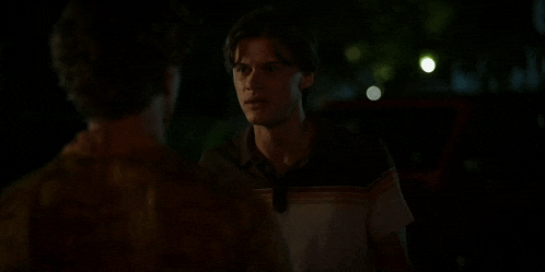 two young men are standing next to each other in the dark and talking to each other .