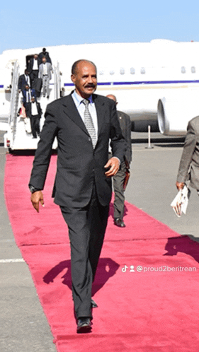a man in a suit walks on a red carpet in front of an airplane