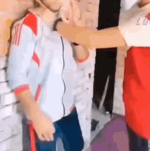 a man in a white and red shirt is being punched in the face by another man in a red shirt .