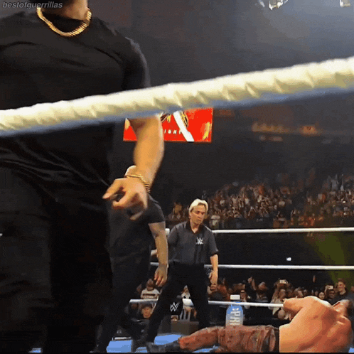 a man in a black shirt stands in a wrestling ring with a referee