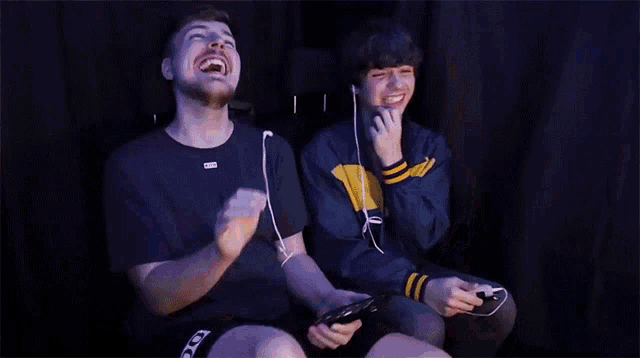 two young men are laughing while playing a video game together .