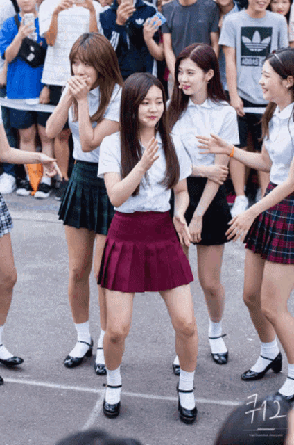 a girl wearing a purple pleated skirt stands in front of a crowd wearing a shirt that says adidas