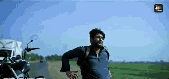 a man walking down a road next to a motorcycle with alt on the bottom