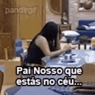 a woman is sitting at a table in a living room with a caption that says pai nosso que estas no ceu .