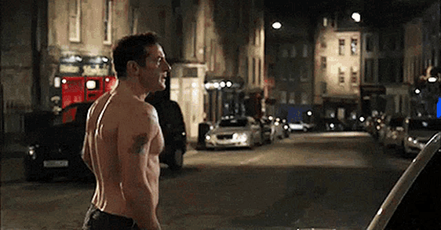 a shirtless man is standing in the middle of a busy street at night .