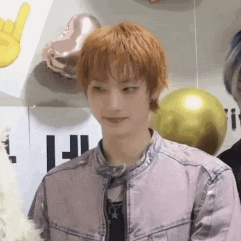a young man with red hair is standing in front of balloons and making a funny face .