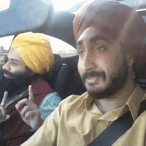 two men wearing turbans are sitting in a car and one is pointing