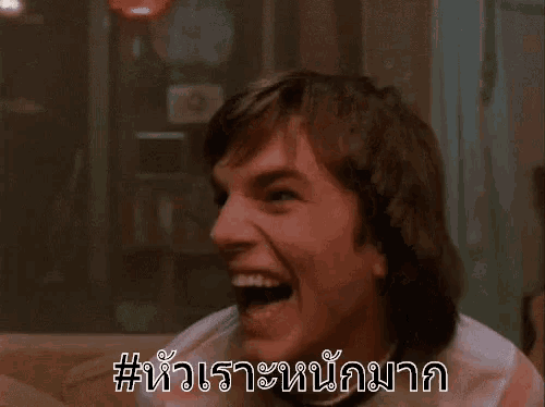 a man is laughing while sitting on a couch in a room with a sign in a foreign language .