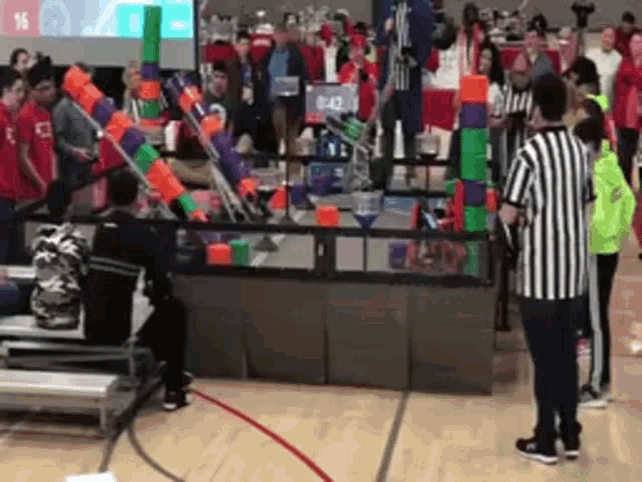 a group of people are playing a game of robotics in a gym while a referee looks on .
