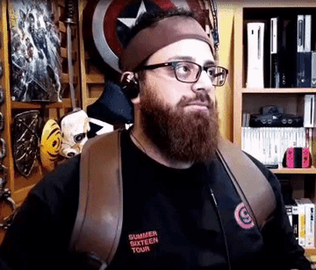 a man with a beard wearing glasses and headphones is standing in front of a bookshelf .