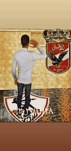 a man standing in front of a brick wall with a red and white emblem that says al ahly