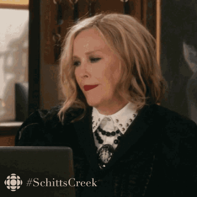 a woman sitting in front of a laptop with #schitts creek on the bottom right