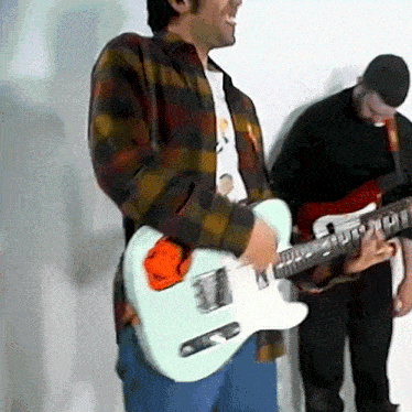 a man in a plaid shirt plays a white guitar