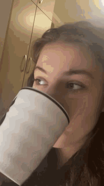 a woman is drinking from a white mug with a black rim