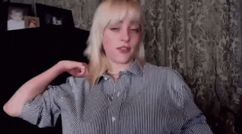 a woman in a striped shirt is standing in front of a curtain and making a funny face .