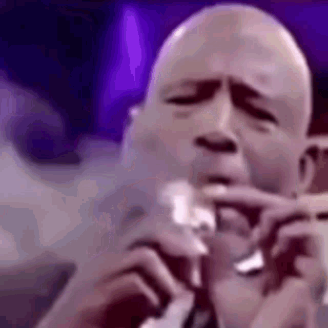 a bald man is singing into a microphone with his eyes closed .