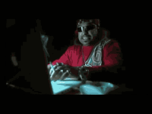a man wearing a red sweater with the letter r on it is looking at a computer screen