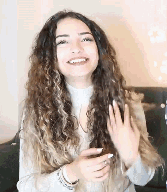 a woman with long curly hair is smiling and holding a cell phone