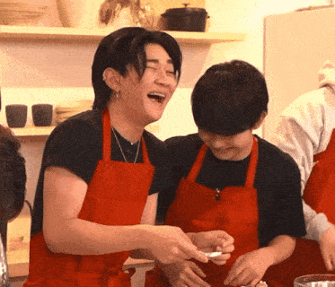 a man and a boy wearing red aprons are laughing in a kitchen