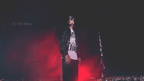 a man wearing sunglasses and a t-shirt that says " live us " stands in front of a city