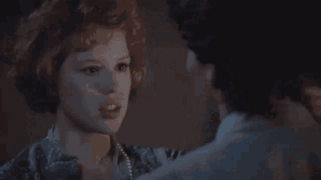 a man and a woman are looking at each other in a dark room . the woman is wearing a pearl necklace .
