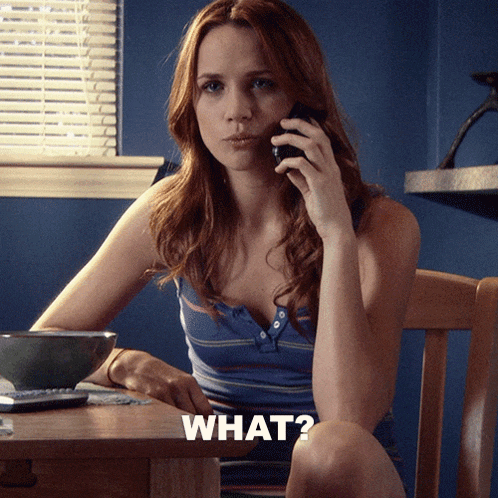 a woman is sitting at a table talking on a cell phone and the word what is on the table in front of her