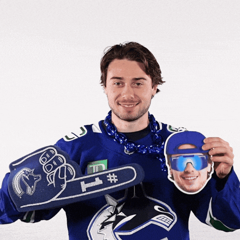 a man wearing a blue hockey jersey holds up a foam hand and a picture of a man wearing sunglasses