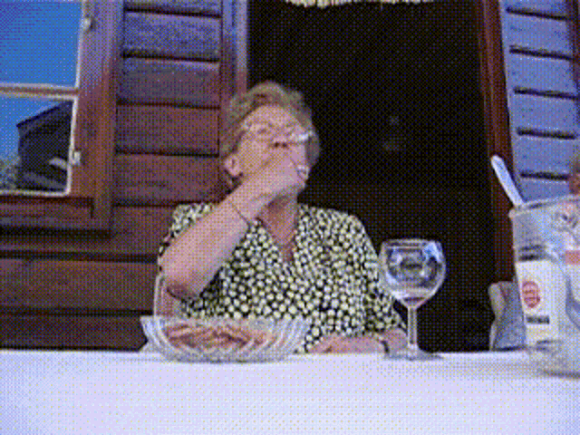 an older woman sitting at a table with a glass of wine and a bowl of food