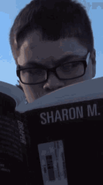 a boy wearing glasses is reading a book by sharon m