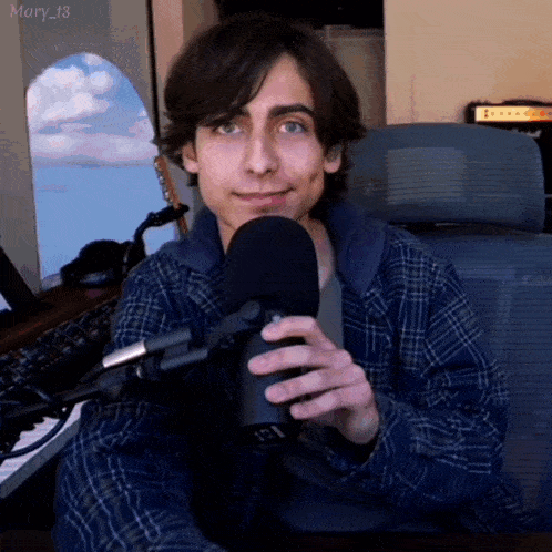a young man in a plaid shirt is holding a microphone and smiling .