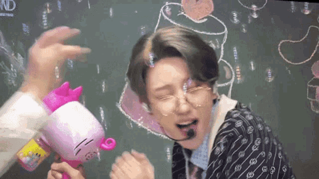 a man is blowing soap bubbles in front of a blackboard with a drawing of a toilet paper roll on it .