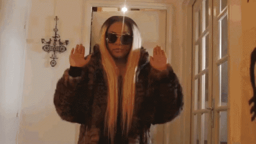 a woman wearing sunglasses and a fur coat is standing in front of a door .