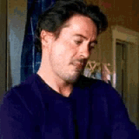 a man in a purple sweater is sitting in front of a window in a room .