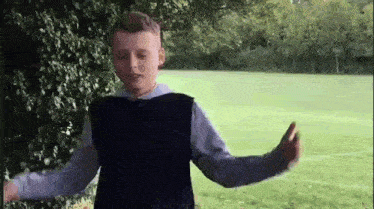 a young boy in a blue vest is standing in a grassy field .