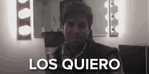 a man is sitting in front of a mirror in a room with the words los quiero written on it .