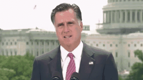 a man in a suit and tie stands in front of microphones
