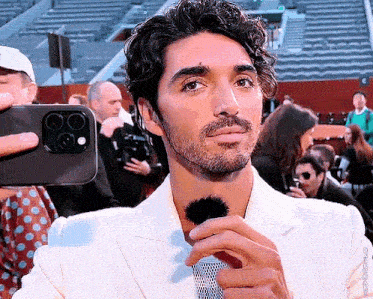 a man in a white suit is holding a microphone and taking a picture with his phone