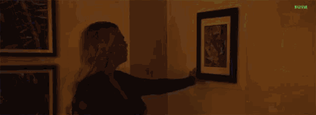a woman is hanging a picture on a wall in a dark room .