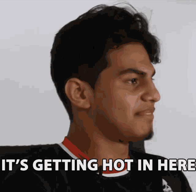 a man is sitting in front of a white wall with the words `` it 's getting hot in here '' written on it .