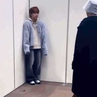 a man is leaning against a wall in a room while a woman looks on .
