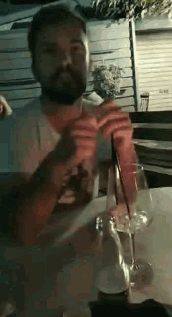 a man with a beard sits at a table with a glass of water and a bottle of soda