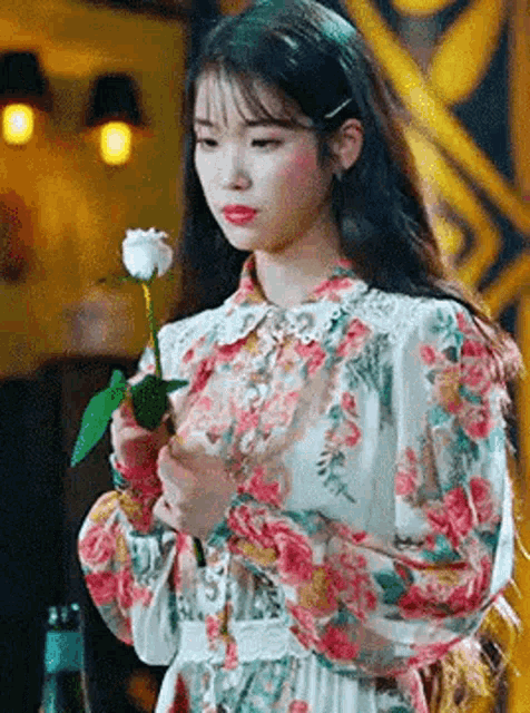 a woman in a floral dress is holding a rose .
