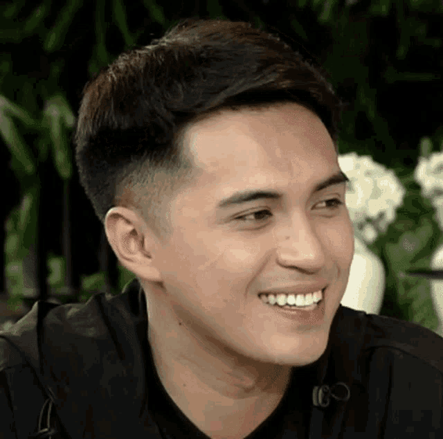 a close up of a man 's face smiling with flowers in the background .
