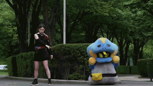 a woman in a black dress stands next to a blue monster